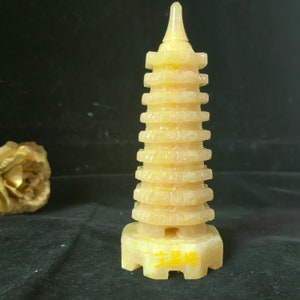 May include: A carved, yellow-toned stone pagoda with multiple tiers and a pointed top. The pagoda has a detailed design and sits on a square base. The text in yellow is visible on the base. The background is dark.