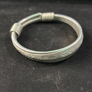 May include: A silver-colored bracelet with intricate floral patterns and a wrapped design. The bracelet has a smooth, polished finish and a classic, timeless appeal. The bracelet is a piece of jewelry.