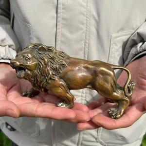 May include: A bronze lion figurine, depicted in a walking pose with its mouth open. The sculpture has a detailed mane and muscular body, showcasing a classic design. The lion is approximately 6 inches long.