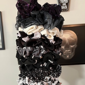 Op de afbeelding: Een stapel van 12 zwarte en witte gepatroneerde scrunchies. De scrunchies hebben verschillende griezelige ontwerpen, waaronder spinnenwebben, schedels en steken.