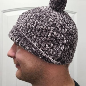 May include: A gray crocheted beanie with a fuzzy texture and a pom-pom on top.