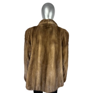 May include: A brown fur coat with a long sleeve and a collar. The coat is on a mannequin.