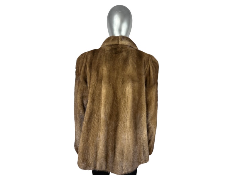May include: A brown fur coat with a long sleeve and a collar. The coat is on a mannequin.