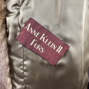 May include: A close-up of a brown fur coat with a burgundy label that reads "Anne Klein II Furs".