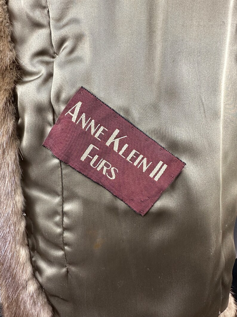 May include: A close-up of a brown fur coat with a burgundy label that reads "Anne Klein II Furs".