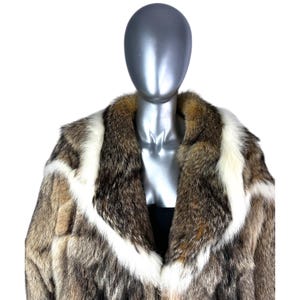 May include: A luxurious fur coat with a striking pattern. The coat features a mix of brown, white, and tan fur, creating a bold visual statement. The design includes a wide collar and a tailored fit, offering a classic and elegant look. The coat is displayed on a mannequin.