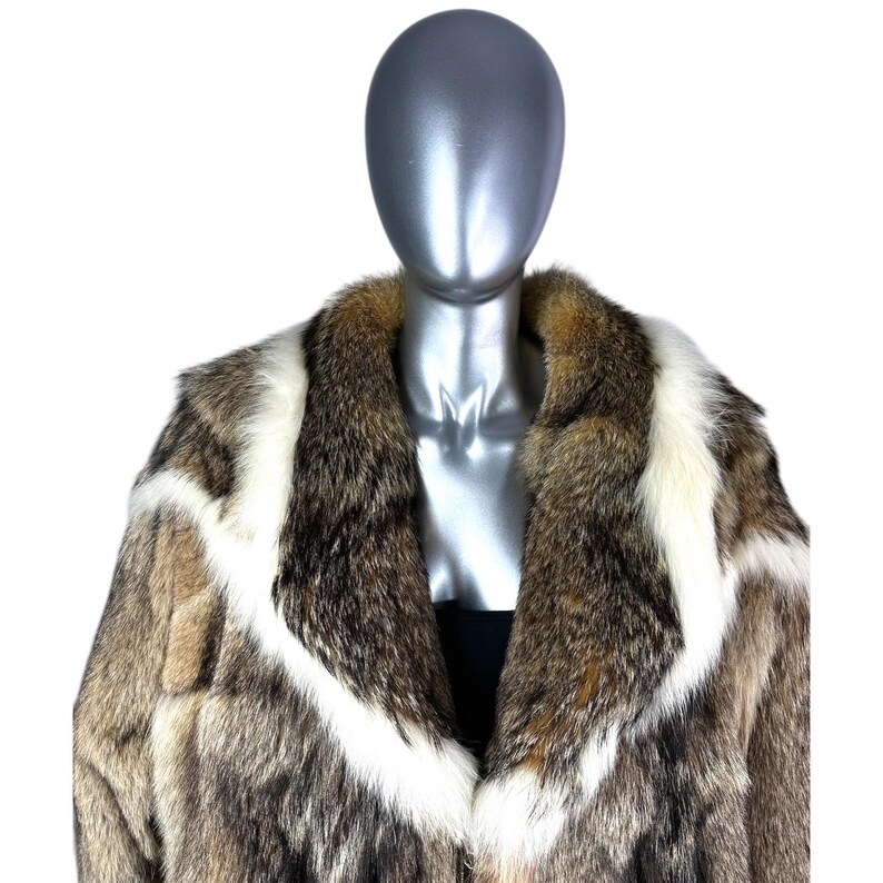 May include: A luxurious fur coat with a striking pattern. The coat features a mix of brown, white, and tan fur, creating a bold visual statement. The design includes a wide collar and a tailored fit, offering a classic and elegant look. The coat is displayed on a mannequin.