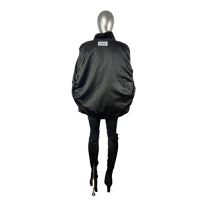 K&ouml;nnte beinhalten: Schwarze Bomberjacke mit Pelzkragen. Die Jacke hat eine Satin-Oberfl&auml;che und ein Etikett auf der R&uuml;ckseite mit der Aufschrift "Echtleder & Pelz."