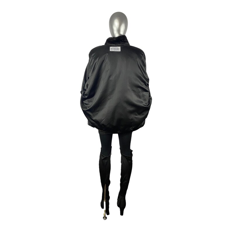 K&ouml;nnte beinhalten: Schwarze Bomberjacke mit Pelzkragen. Die Jacke hat eine Satin-Oberfl&auml;che und ein Etikett auf der R&uuml;ckseite mit der Aufschrift "Echtleder & Pelz."