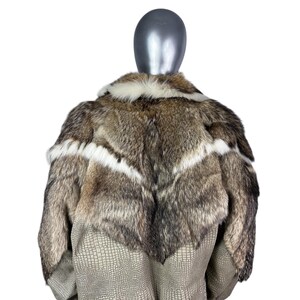 May include: A luxurious fur coat displayed on a mannequin. The coat features a mix of brown, gray, and white fur with a chevron design. The lower portion of the coat has a textured, light brown, faux-leather material.