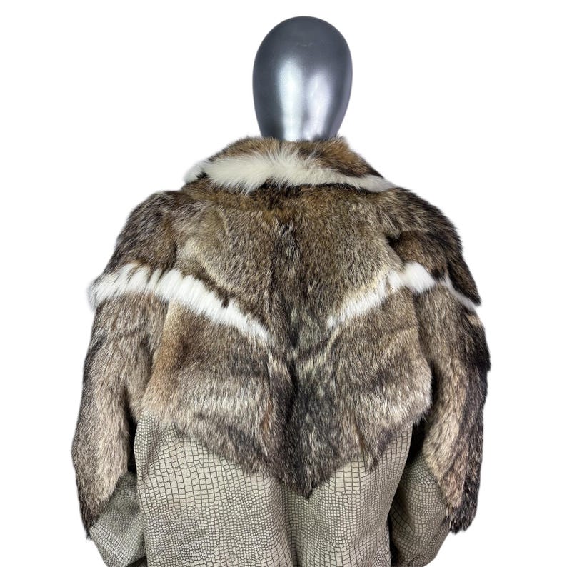 May include: A luxurious fur coat displayed on a mannequin. The coat features a mix of brown, gray, and white fur with a chevron design. The lower portion of the coat has a textured, light brown, faux-leather material.