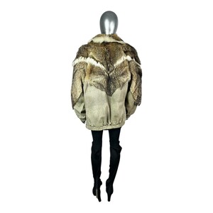 May include: A tan and brown jacket with a fur collar and accents. The jacket has a textured pattern on the lower portion and a zipper closure. The model is wearing black pants and boots.