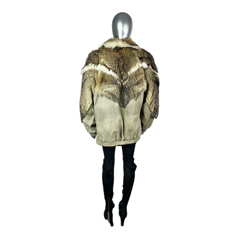 May include: A tan and brown jacket with a fur collar and accents. The jacket has a textured pattern on the lower portion and a zipper closure. The model is wearing black pants and boots.