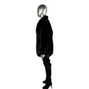 K&ouml;nnte beinhalten: Eine schwarze Kunstfelljacke mit langer, lockerer Passform. Die Jacke hat einen Stehkragen und einen Rei&szlig;verschluss.