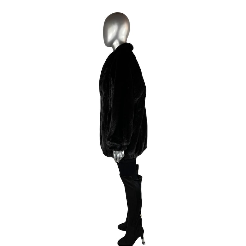K&ouml;nnte beinhalten: Eine schwarze Kunstfelljacke mit langer, lockerer Passform. Die Jacke hat einen Stehkragen und einen Rei&szlig;verschluss.