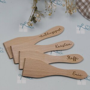 Könnte beinhalten: Vier Holzspatel mit gravierten Namen, darunter "Lieblingsgast", "Karsten", "Steffi" und "Eric".