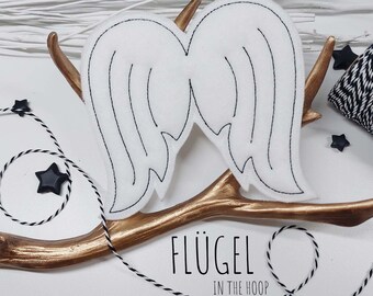May include: White felt angel wings with black stitching, displayed on a gold branch. The text "FLÜGEL IN THE HOOP" is below the wings. The text "7 GRÖBEN IM SET / CHIMBEERDESIGN" is below the text "IN THE HOOP". The text "FÜR DIE RAHMENGRÖBEN 10X10/13X18/14X20/15x24/16X26 UND 18X30" is below the text "CHIMBEERDESIGN".