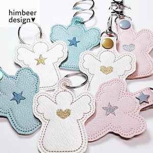 Könnte beinhalten: Fünf engelartige Schlüsselanhänger in verschiedenen Farben und Designs. Die Schlüsselanhänger sind aus Kunstleder gefertigt und haben goldene Akzente. Die Schlüsselanhänger zeigen ein Stern- oder Herzdesign.