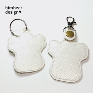 May include: Two white leather keyrings shaped like paw prints. One keyring has a silver ring and the other has a silver ring with a gold metal button.