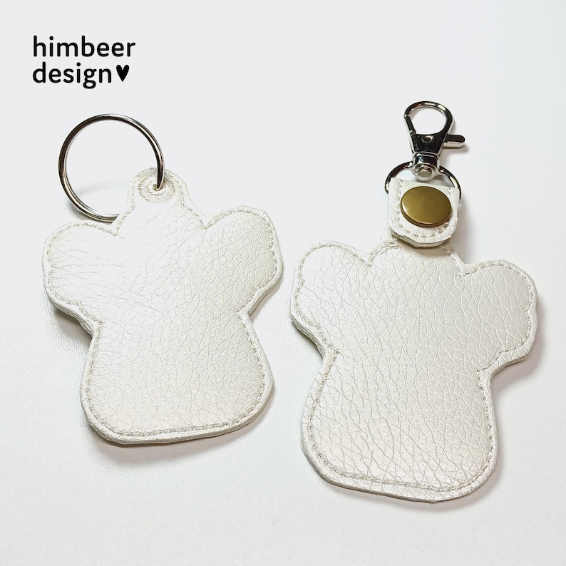 May include: Two white leather keyrings shaped like paw prints. One keyring has a silver ring and the other has a silver ring with a gold metal button.