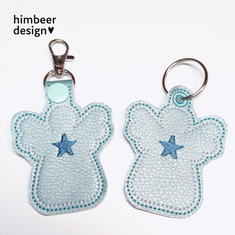 May include: Two light blue angel-shaped keyrings with a blue star in the centre. The keyring on the left has a silver split ring and a light blue swivel clip. The keyring on the right has a silver split ring.