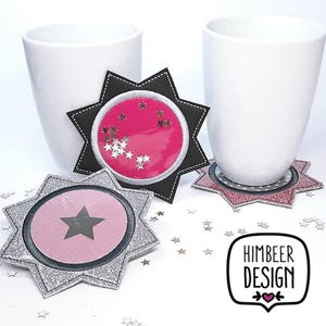 May include: Two white ceramic mugs with silver glitter star-shaped coasters. The coasters have a pink center with silver glitter stars. The coasters are on a white surface with silver glitter stars scattered around them.
