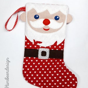 Puede incluir: Calcetín de Navidad rojo y blanco con una cara de Papá Noel de fieltro blanco y un cinturón de fieltro marrón. El calcetín está decorado con corazones blancos.