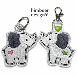Puede incluir: Dos llaveros con forma de elefante plateado con orejas gris oscuro y contornos cosidos. Uno tiene un corazón rosa, el otro un corazón verde y un mosquetón de metal. El texto 'himbeer design' con un símbolo de corazón está centrado arriba.