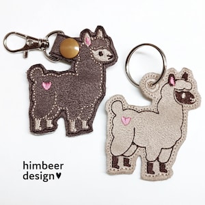 Può includere: Due portachiavi a forma di lama. Uno è marrone scuro con una chiusura argentata e un cuore rosa. L'altro è beige chiaro con un portachiavi argentato e un cuore rosa. Il testo "himbeer design" è in basso.