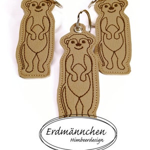 Könnte beinhalten: Drei braune Leder-Schlüsselanhänger mit gestickten Erdmännchen. Die Schlüsselanhänger sind an silbernen Schlüsselringen befestigt. Der Text "Erdmännchen Himbeerdesign" ist auf einem weißen ovalen Etikett gedruckt.