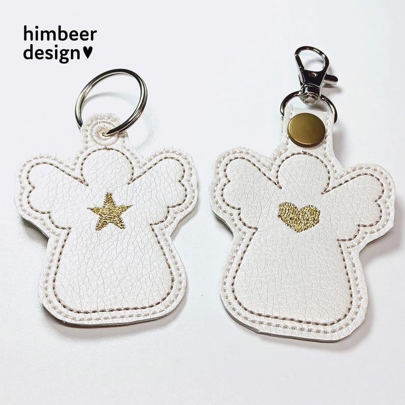 May include: Two white angel keyrings with gold embroidery. One angel has a star and the other has a heart.