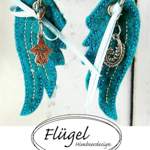 Könnte beinhalten: Zwei Flügel aus türkisfarbenem Filz mit silbernen Schlüsselanhängern. Ein Schlüsselanhänger hat einen Anhänger mit der Aufschrift "Made for an Angel" und der andere einen Federanhänger. Die Flügel sind mit einem weißen Band zusammengebunden.