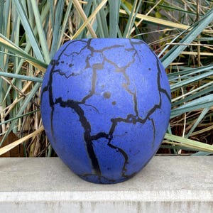 May include: A blue ceramic vase with a crackle glaze and black lines. The vase is round and has a smooth surface.