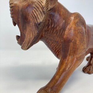 May include: A hand-carved wooden sculpture of a tiger with its mouth open in a roar. The sculpture is made of dark brown wood and has a realistic appearance.