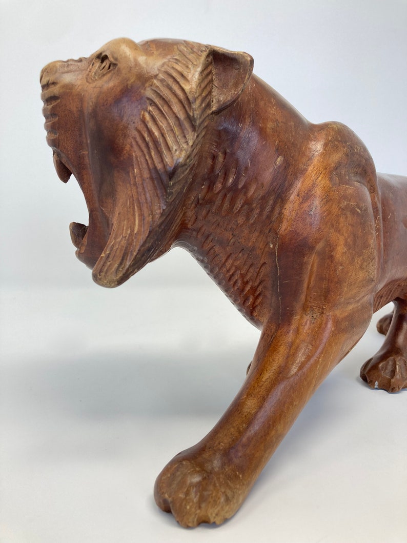 May include: A hand-carved wooden sculpture of a tiger with its mouth open in a roar. The sculpture is made of dark brown wood and has a realistic appearance.