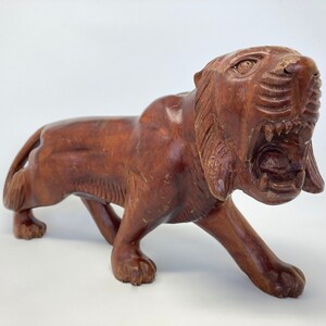 May include: A hand-carved wooden tiger figurine with a snarling expression. The tiger is brown and has detailed carvings on its fur and face.