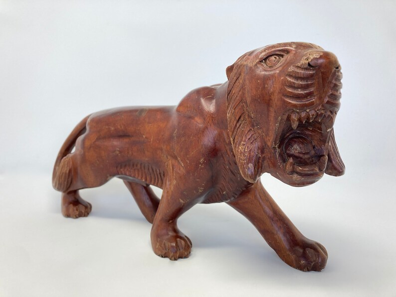 May include: A hand-carved wooden tiger figurine with a snarling expression. The tiger is brown and has detailed carvings on its fur and face.
