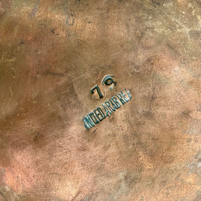 May include: Close-up of a copper-coloured surface with the number "79" and the words "United Arab Rep" stamped in black.