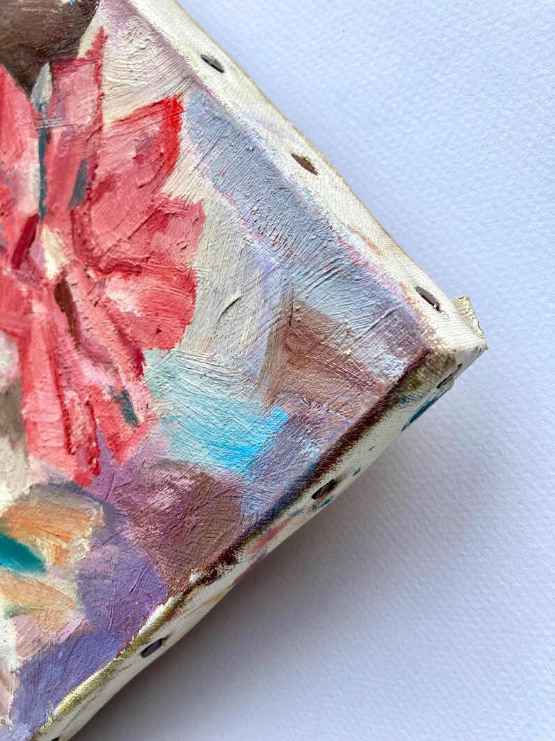 May include: Close-up of a colorful abstract painting on a stretched canvas. The painting features a pink flower with blue and white accents. The canvas is secured with staples and has a textured surface.
