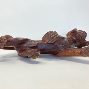 May include: A hand-carved wooden sculpture of a brown lion in a crouching position. The lion's head is turned to the side and its mouth is open. The sculpture is detailed with carved fur and claws.