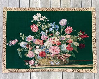 May include: A tapestry wall hanging with a green background and a woven image of a basket overflowing with colorful flowers. The basket is made of woven brown material and the flowers are in shades of pink, red, white, and blue.