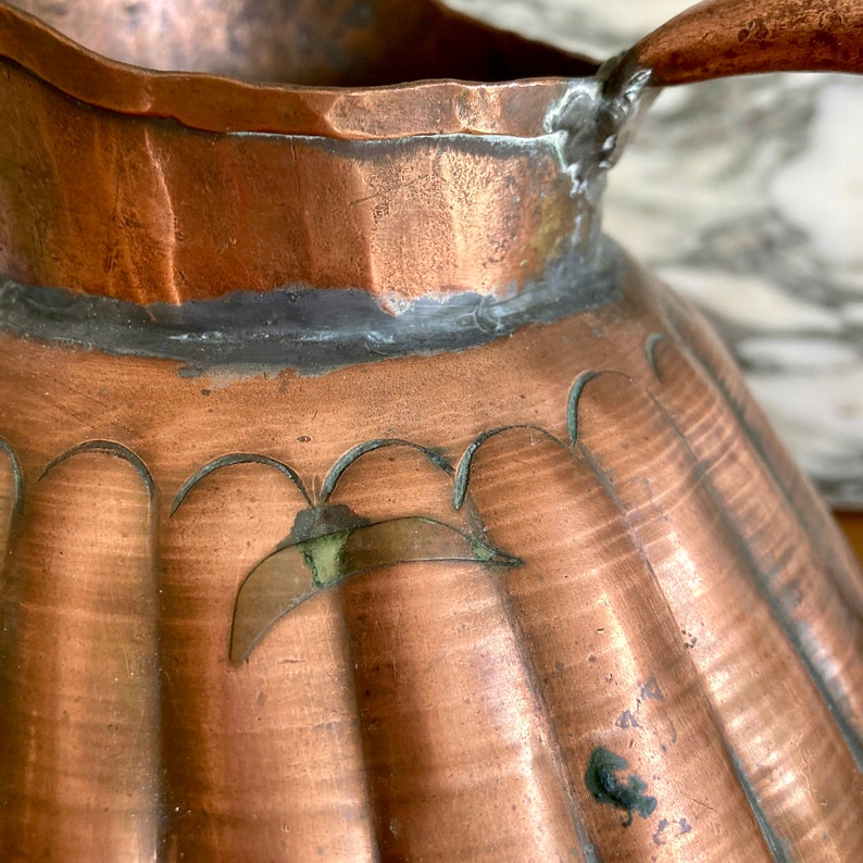 May include: A copper jug with a fluted design and a decorative handle. The jug has a green patina on the surface.
