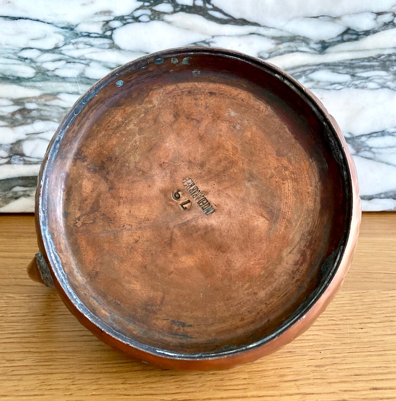 May include: The underside of a copper kettle with a maker's mark that reads "Made in France" and the number "91".