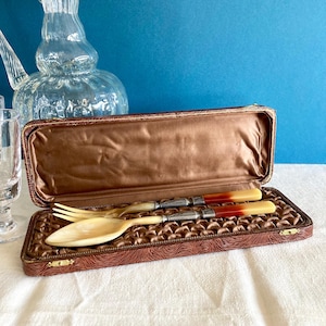 Peut inclure: Un coffret en similicuir marron avec une doublure en velours, contenant un service à salade vintage en argent plaqué avec des manches en ivoire. Les manches ont un motif marbré rouge et jaune.
