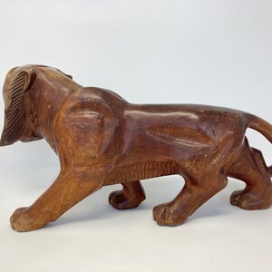 May include: A carved wooden lion figurine in a walking pose. The lion is brown and has a detailed mane. The figurine is made of dark wood and has a smooth finish.