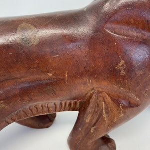 May include: A dark brown wooden sculpture of a lion in a standing position. The lion has detailed carvings on its body and paws.