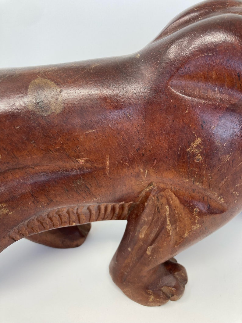 May include: A dark brown wooden sculpture of a lion in a standing position. The lion has detailed carvings on its body and paws.
