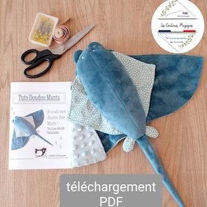 Puede incluir: Un juguete de peluche azul con forma de manta raya con un ala estampada, tijeras, alfileres y un patrón de costura titulado "Tuto Doudou Manta". El patrón incluye instrucciones y el texto "Je couds mon doudou Raie Manta!" Descarga PDF.