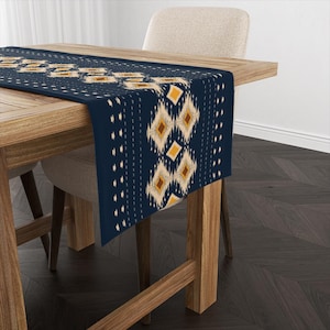 May include: A navy blue table runner with a geometric pattern in shades of beige, brown, and yellow. The runner is on a wooden table with a chair.