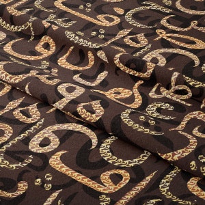 May include: Brown fabric with a repeating pattern of black and yellow stylised letters. The fabric is folded in half, showing the pattern on both sides.